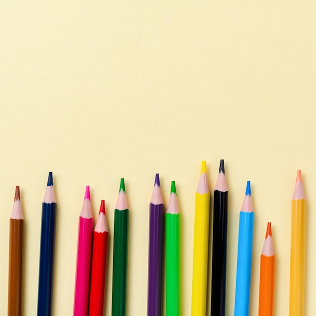 Multicolored wooden pencils for school on yellow paper background. School and office stationery on yellow background. Concept back to school. Square image. Top view.