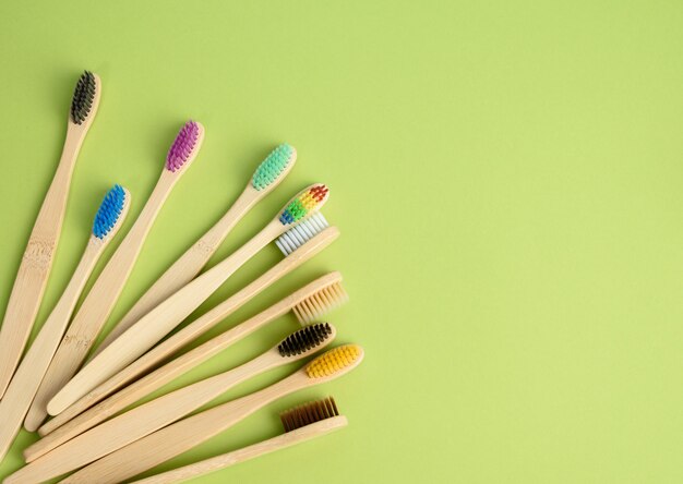 Multicolored wooden toothbrushes on a green background, plastic rejection concept, zero waste, top view