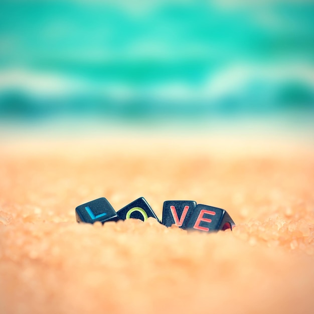 Foto parola multicolore amore da cubi neri nella sabbia sullo sfondo della spiaggia e del mare tonica