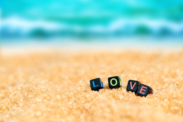 Photo multicolored word love from black cubes in the sand on the background of beach and sea