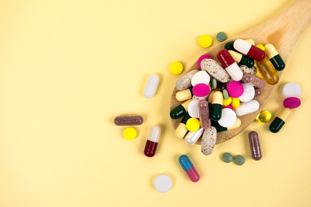 Multicoloured pills and capsules in a wooden spoon and next to it on a beige background