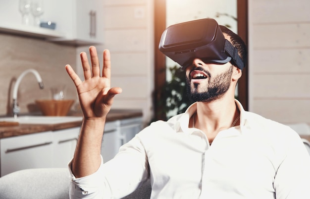 Multicultural bearded man getting experience using VRheadset glasses of virtual reality much gesticulating hands on the modern flat background