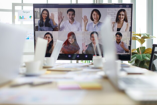Photo multicultural businesspeople in company say hi waving hand greeting each other in global video conference corporate sales target report meeting on computer monitor in office room with laptop on table.