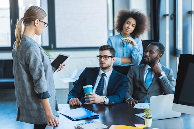 Multicultural businesspeople looking at businesswoman with tablet in office