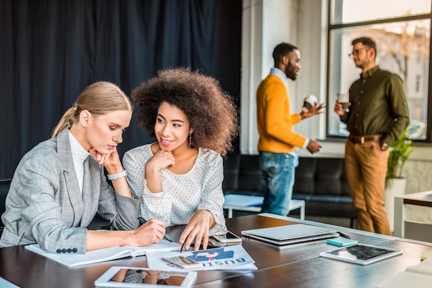 Photo multicultural businesswomen talking at table in office