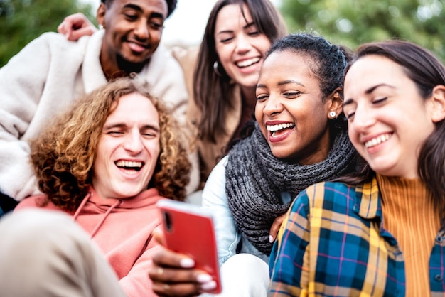 Amici multiculturali che si divertono con il cellulare nel cortile urbano