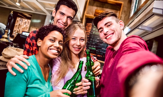 Multicultural friends taking selfie and drinking beer at fancy brewery restaurant