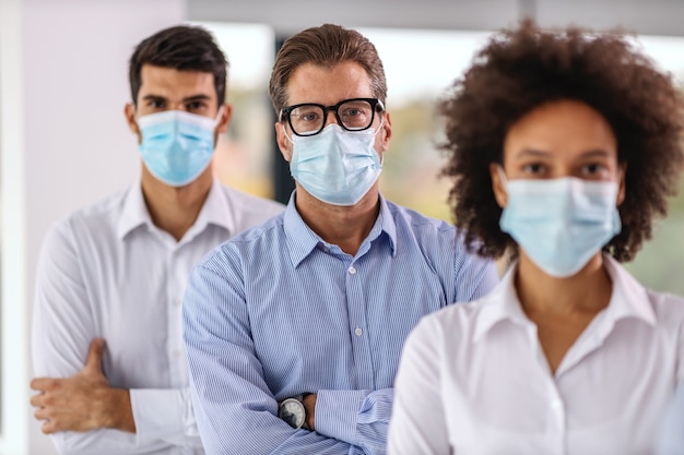 Photo multicultural group of business people with face masks standing with arms crossed in corporate firm.