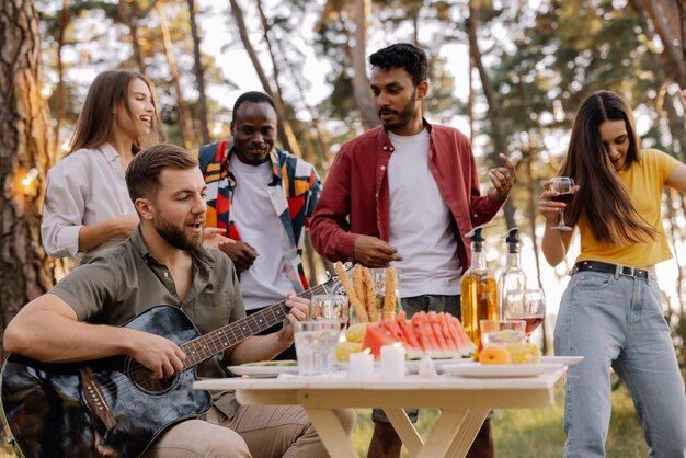 Multicultural group of people bearded hipster man playing guitar and friends dancing and having fun