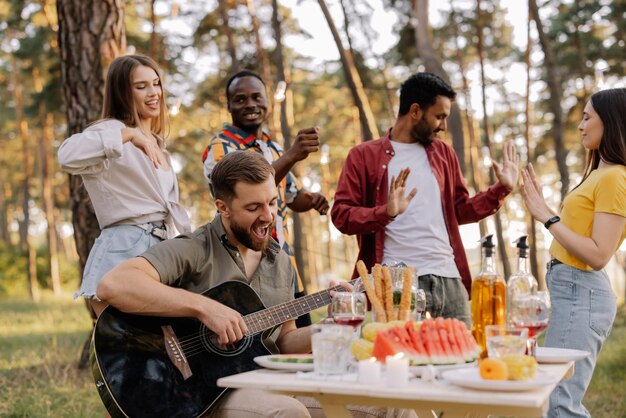 Foto gruppo multiculturale di persone hipster barbuto che suona la chitarra e amici che ballano e si divertono