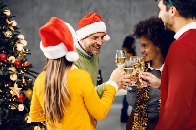 Un gruppo multiculturale in piedi accanto a un albero di natale in casa e brindando alla vigilia di capodanno