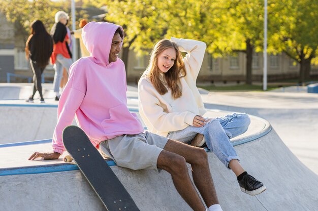 Multicultural group of young friends bonding outdoors and having fun - Stylish cool teens gathering at urban skate park