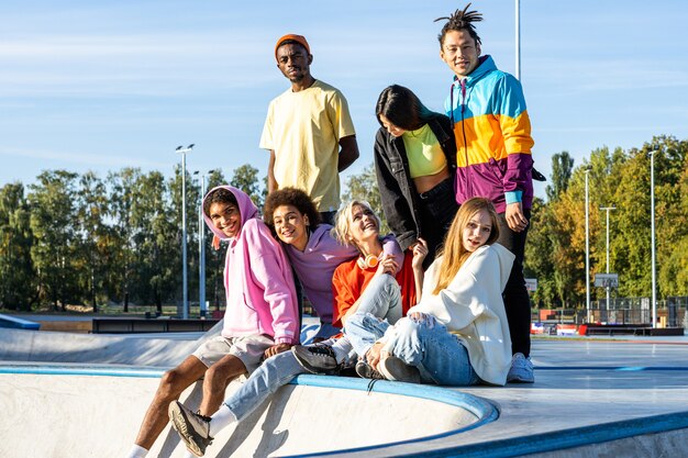 Gruppo multiculturale di giovani amici che si uniscono all'aperto e si divertono - ragazzi alla moda e alla moda che si riuniscono allo skate park urbano