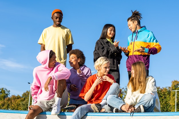 Gruppo multiculturale di giovani amici che si uniscono all'aperto e si divertono - ragazzi alla moda e alla moda che si riuniscono allo skate park urbano