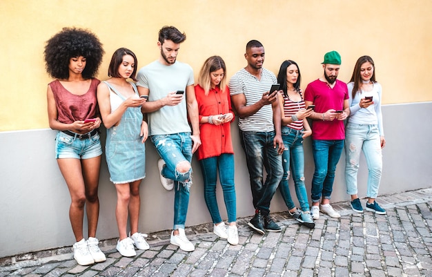 Multicultural milenials using smartphone against wall at university college backyard