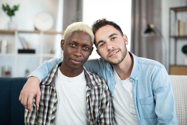 Foto multicultureel stel van hetzelfde geslacht knuffelen en glimlachen op de bank