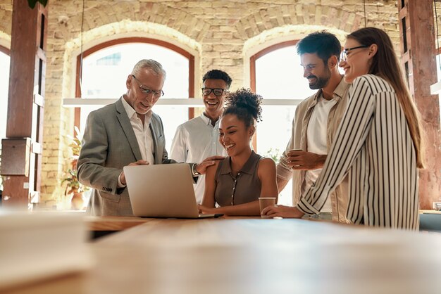 multicultureel team dat naar de laptop kijkt en iets bespreekt terwijl ze samen op kantoor werken