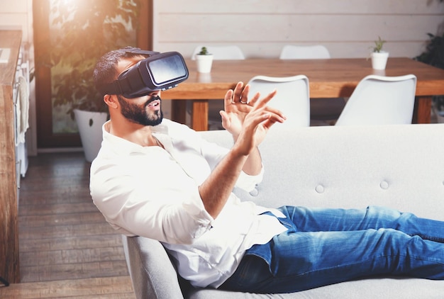 Foto multiculturele bebaarde man die op de bank ligt en een virtual reality-bril gebruikt in de moderne flat