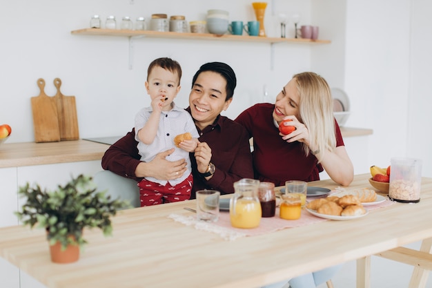 Multiculturele gelukkige familie. Aziatische vader en zijn blanke blonde vrouw ontbijten met hun mooie zoon in de keuken.