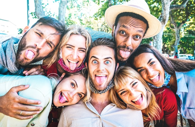 Multiculturele vrienden die een gekke selfie nemen terwijl ze hun tong uitsteken tijdens de derde golf van Covid 19