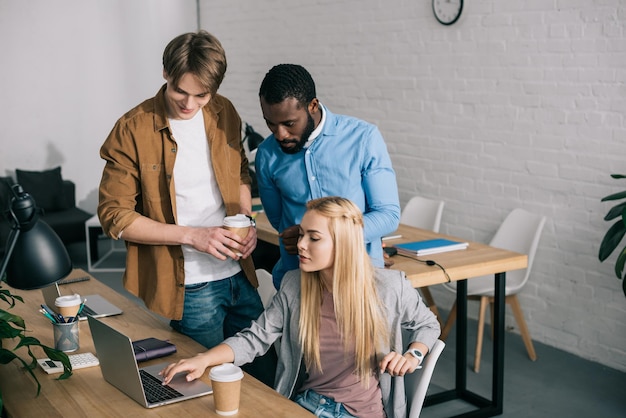 Multiculturele zakelijke collega's met koffiekopjes praten en kijken op laptop