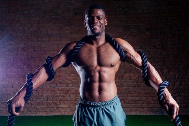 Multiethnic bare sexy chest sportsmen exercising with battle ropes at the gym