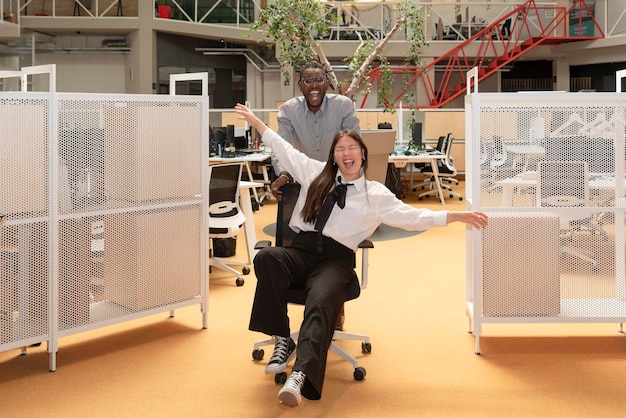 Multiethnic business colleagues having fun in the work break sitting in the office wheelchair in a coworking space