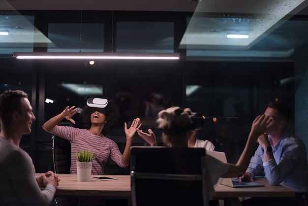 Multiethnic Business team using virtual reality headset in night office meeting  Developers meeting with virtual reality simulator around table in creative office.