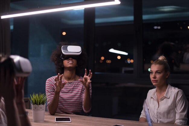 Multiethnic Business team using virtual reality headset in night office meeting  Developers meeting with virtual reality simulator around table in creative office.