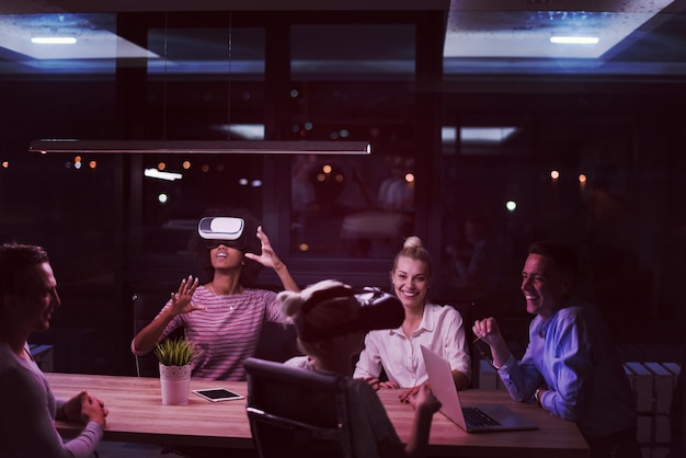 Multiethnic Business team using virtual reality headset in night office meeting  Developers meeting with virtual reality simulator around table in creative office.