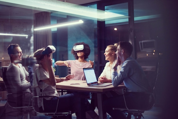 Multiethnic Business team using virtual reality headset in night office meeting  Developers meeting with virtual reality simulator around table in creative office.