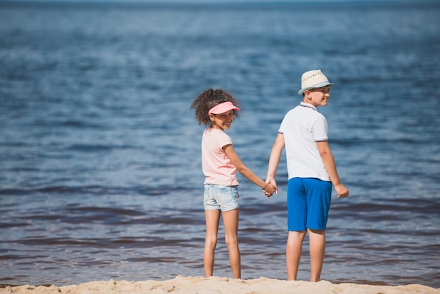 海辺で一緒に立っている間手を繋いでいる多民族の子供たち