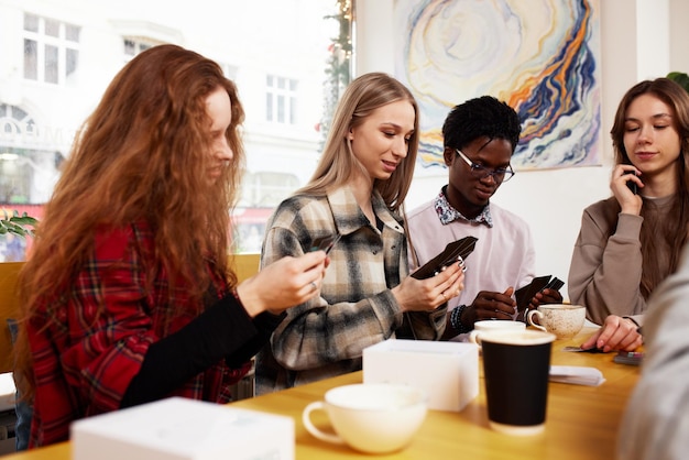 Multiethnic company of young people drinking coffee and playing games looking at smartphones taking