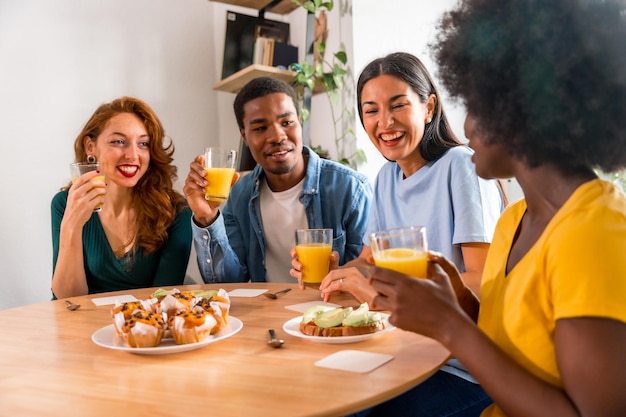 Amici multietnici che si divertono a fare colazione con succo d'arancia e muffin a casa