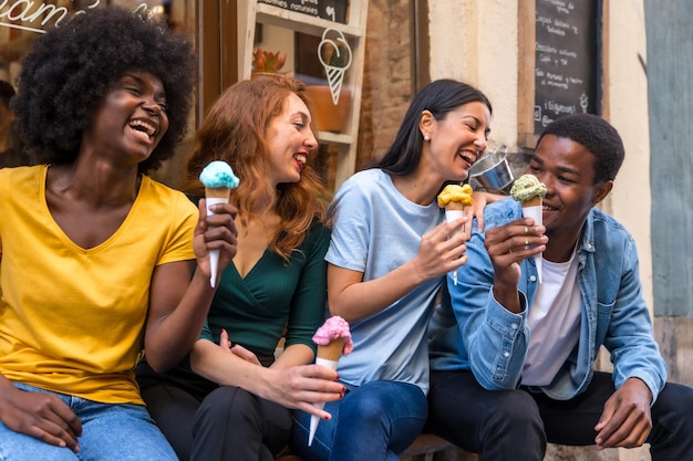 Amici multietnici in una gelateria che mangiano un gelato divertimento estivo sorridente