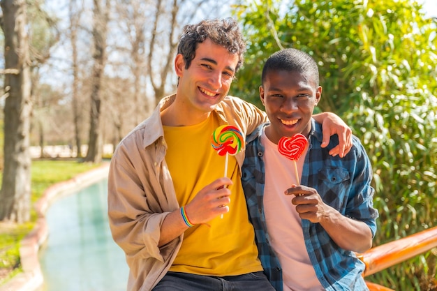 Coppia gay multietnica che mangia un lecca-lecca concetto lgbt divertimento romantico in natura