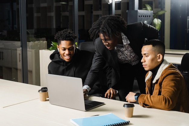 Multiethnic group of African and Asian colleagues are working on laptop on business project Two black handsome managers teamwork with an Asian man and create creative ideas