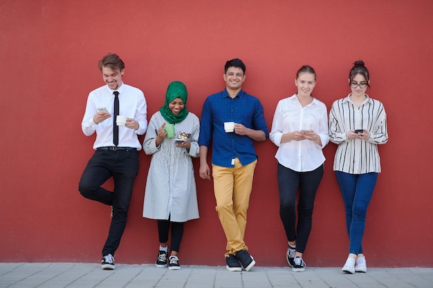 multiethnic group of casual business people using mobile phone during coffee break from work in front of pink wall outside