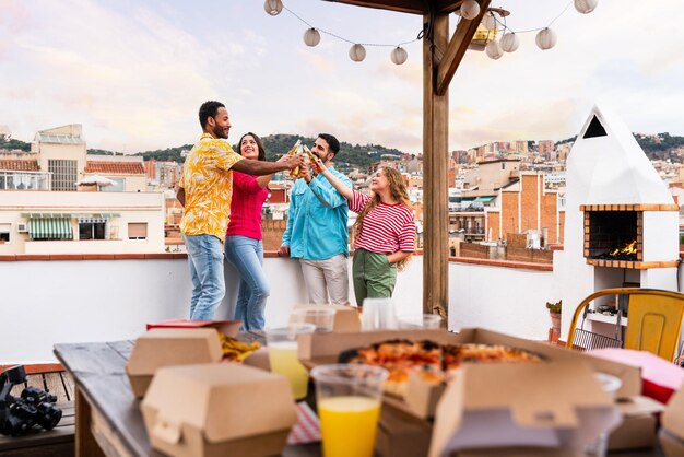 Multiethnic group of happy young friends having dinner barbecue party on rooftop at home