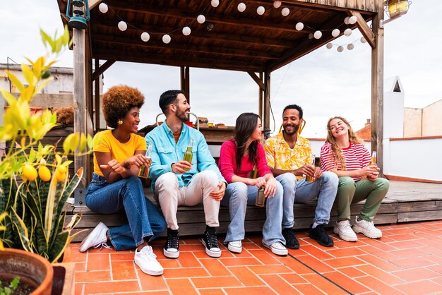 Multiethnic group of happy young friends having dinner barbecue party on rooftop at home