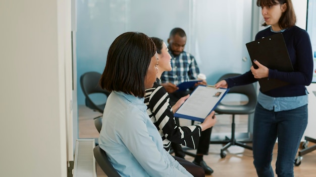 Multiethnic group of people receiving cv papers and waiting to start corporate job interview. Stressed applicants with business career opportunity sitting in queue to attend hiring meeting.