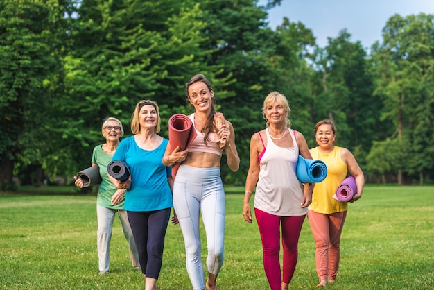 フィットネスインストラクターと一緒に公園でトレーニングする年配の女性の多民族グループ-自然の中でスポーツをしているアクティブな高齢者