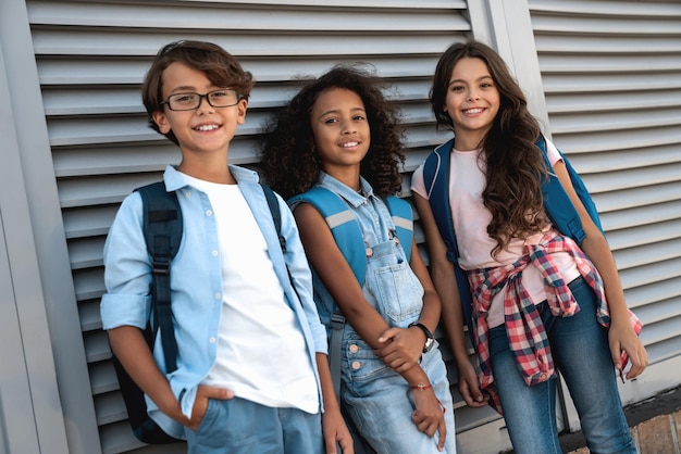 Multiethnic group of smiling school kids looking in camera at the street standing over grey