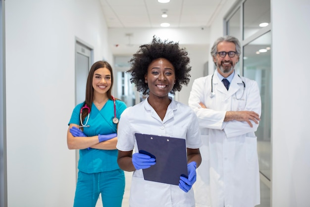 A multiethnic group of three doctors and nurses standing in a hospital corridor wearing scrubs and coats The team of healthcare workers are staring at the camera and smiling