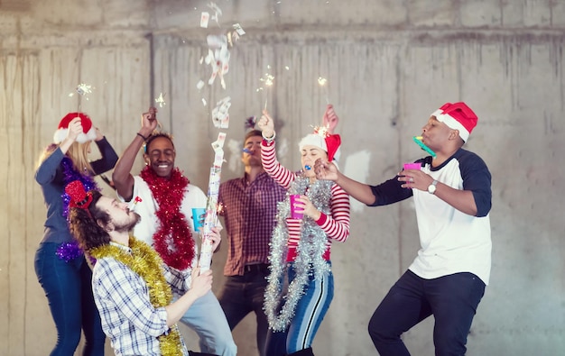 multiethnic group of young happy casual business people dancing and having confetti party while celebrating new year eve in front of concrete wall at new startup office