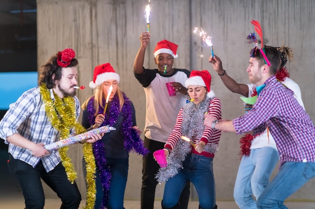 multiethnic group of young happy casual business people dancing with sparklers and having fun while celebrating new year eve in front of concrete wall at new startup office