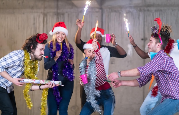 multiethnic group of young happy casual business people dancing with sparklers and having fun while celebrating new year eve in front of concrete wall at new startup office