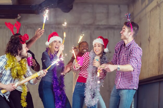 multiethnic group of young happy casual business people dancing with sparklers and having fun while celebrating new year eve in front of concrete wall at new startup office