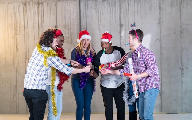 multiethnic group of young happy casual business people lighting a sparkler and having fun while celebrating new year eve in front of concrete wall at new startup office