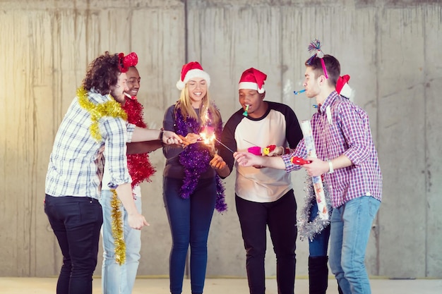 multiethnic group of young happy casual business people lighting a sparkler and having fun while celebrating new year eve in front of concrete wall at new startup office